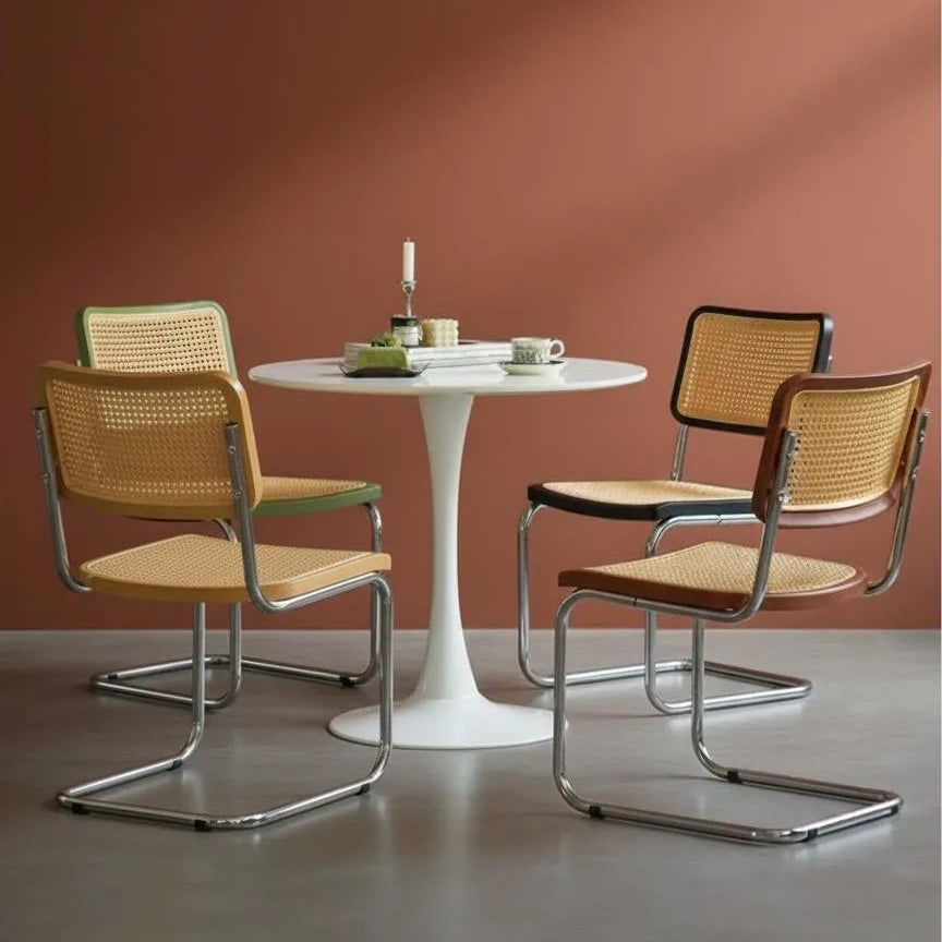 Round white table with four chairs featuring wicker backs and metal frames against a brown wall.