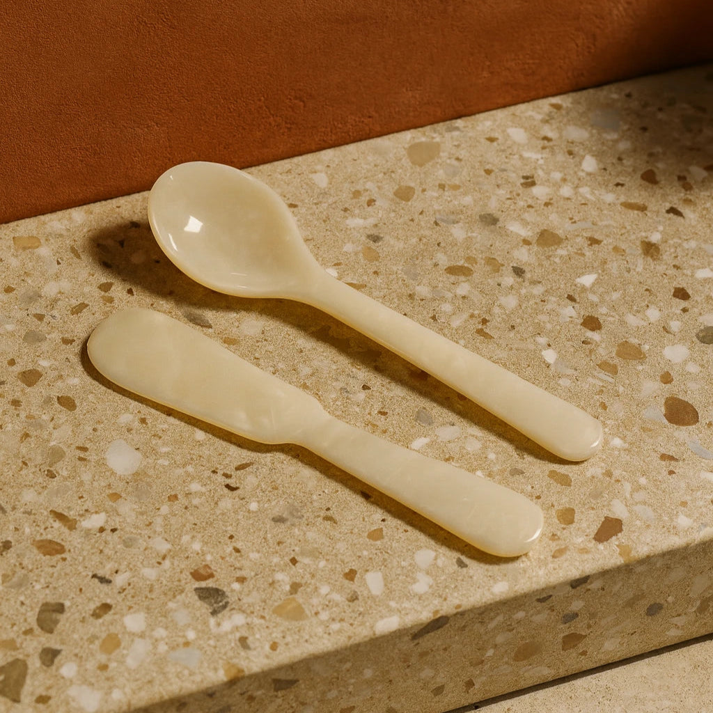 Two beige ceramic spoons on a terrazzo countertop with a brown background