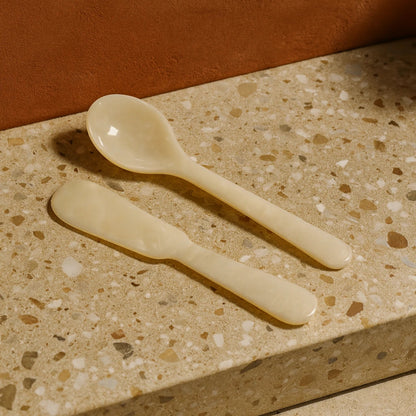 Two beige ceramic spoons on a terrazzo countertop with a brown background