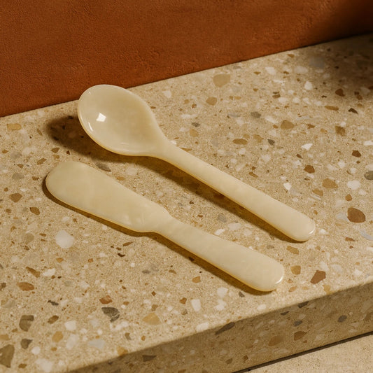 Two beige ceramic spoons on a terrazzo countertop with a brown background