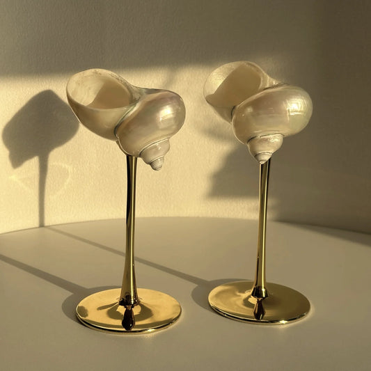 Two shell-shaped candle holders with gold stands on a neutral background