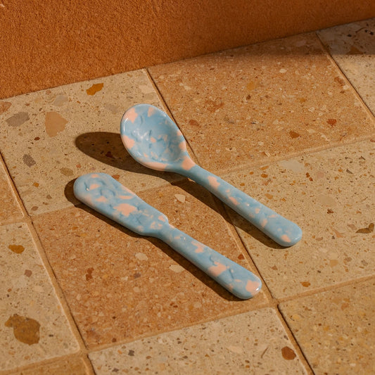 Two blue spoons with pink polka dots on a beige tiled floor.