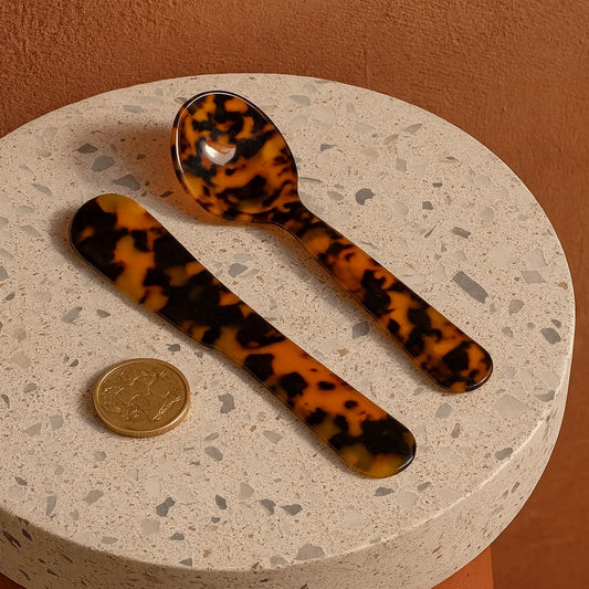 Two tortoiseshell spoons on a terrazzo surface with a coin for scale against a brown background