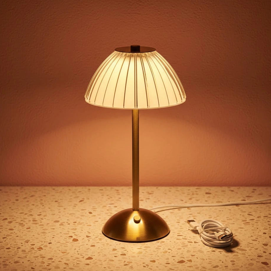 A glass fluted table lamp on a terazzo work surface omitting a warm light with a charging wire next to it.