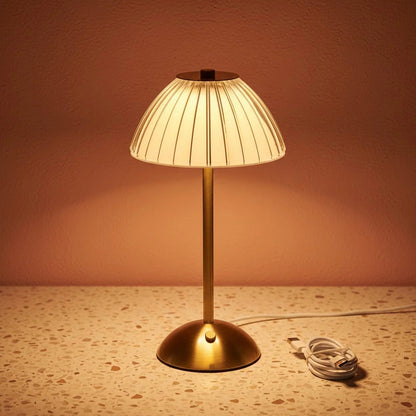 A glass fluted table lamp on a terazzo work surface omitting a warm light with a charging wire next to it.