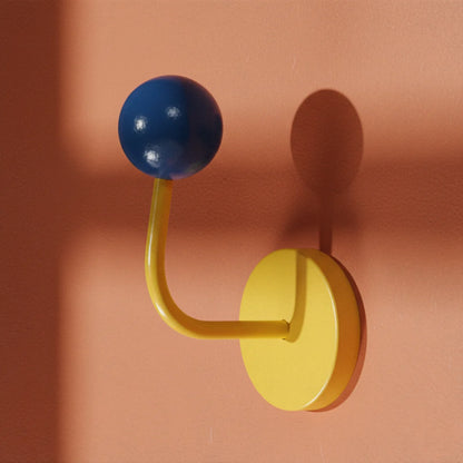 Yellow wall hook with a blue ball on a peach-colored background