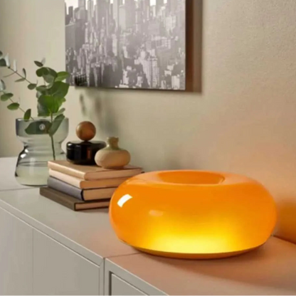 Orange table lamp on a surface with decorative items and a cityscape painting in the background.